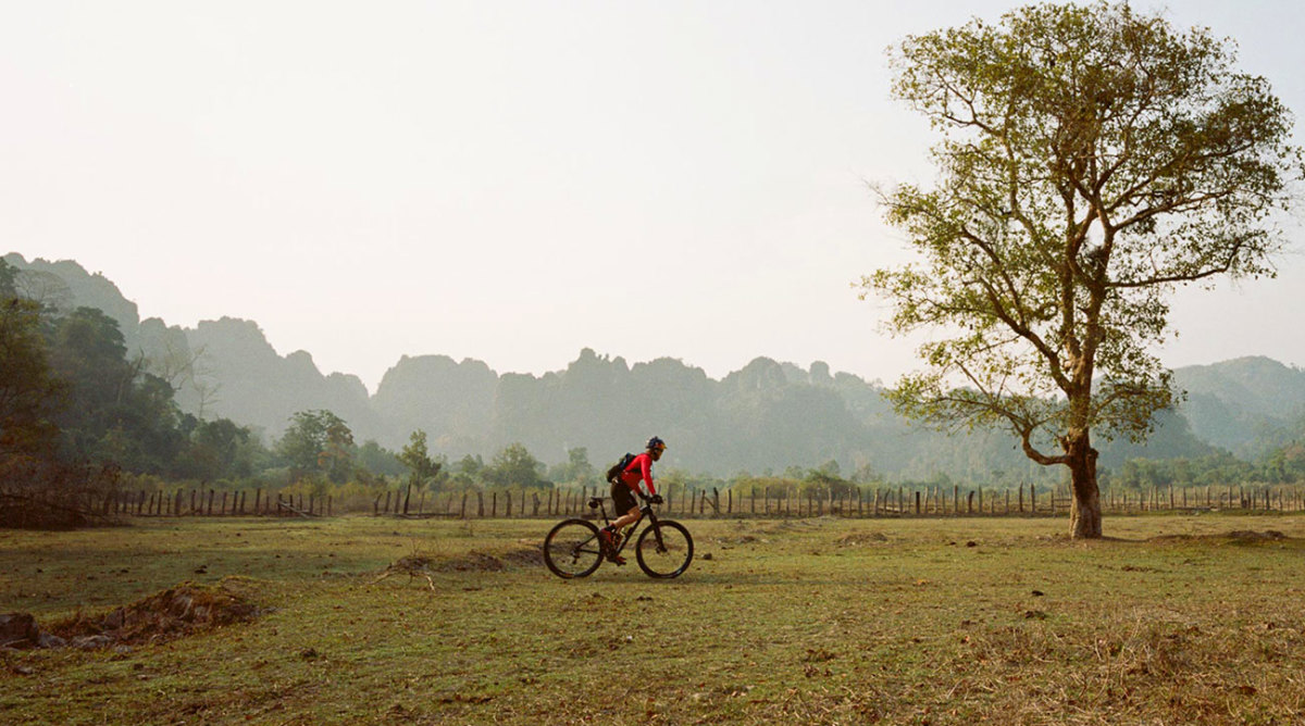 Rebecca cycling across a field in Laos. From the ride along the Ho Chin Minh Trail in 2015.